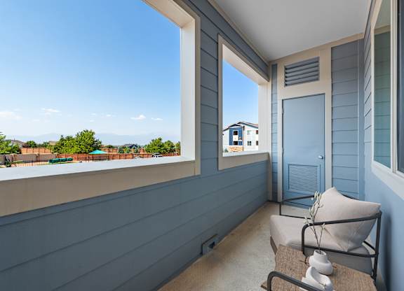 A balcony with a chair and a table with a vase of flowers on it.