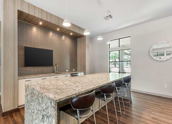 A modern kitchen with a long marble island and a flat screen TV mounted on the wall.