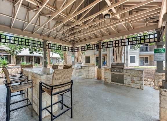 A patio with a table and chairs under a wooden roof.
