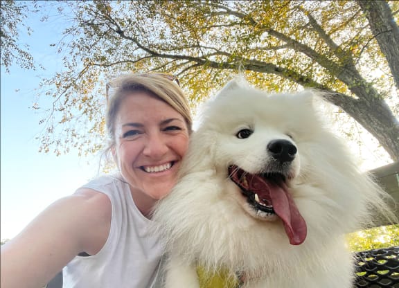 a woman holding a white dog with its tongue out