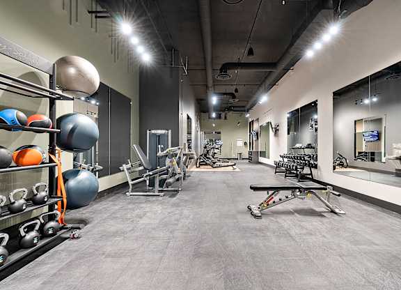 A gym with a variety of equipment including weights and a bench press.at Raymond Block, Edmonton Alberta T6E 3R7