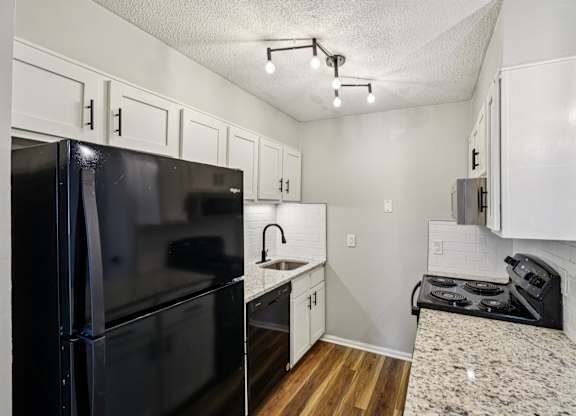 A black fridge and stove in a small kitchen.