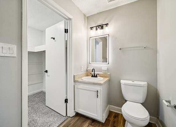 A white bathroom with a toilet, sink, mirror, and a door.