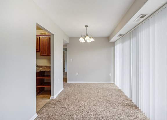 a hallway with white curtains and a carpeted floor and a door to a kitchen at Andrews Ridge Apartments, Suitland, MD