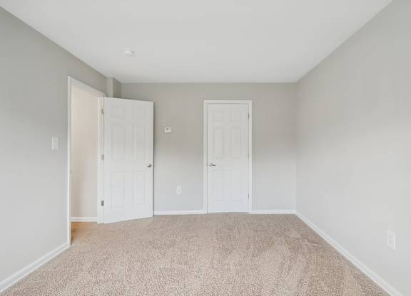 an empty bedroom with two doors and a carpeted floor at Andrews Ridge Apartments, Suitland, MD