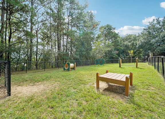 A wooden bench sits in the middle of a grassy area with trees in the background.