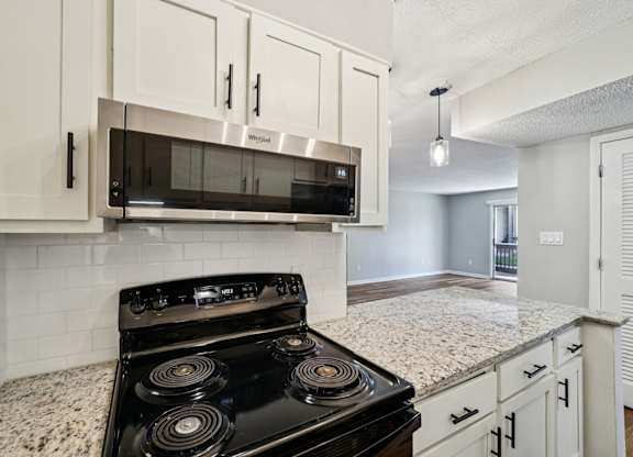 A black stove top oven with four burners is in a kitchen with white cabinets.