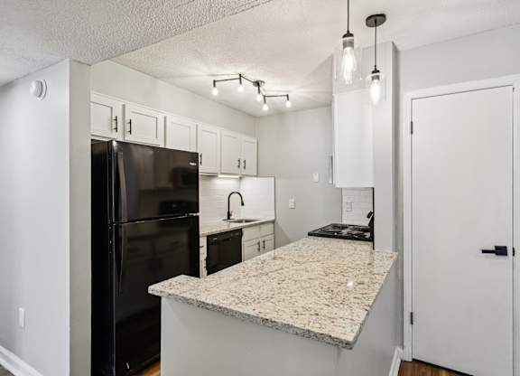 A kitchen with a granite countertop and a black refrigerator.