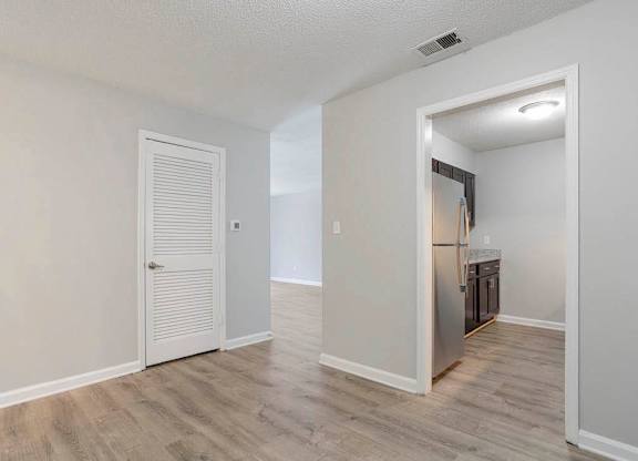 A room with a white door and a kitchen area in the background. at The Onyx Hoover Apartments, Hoover, AL