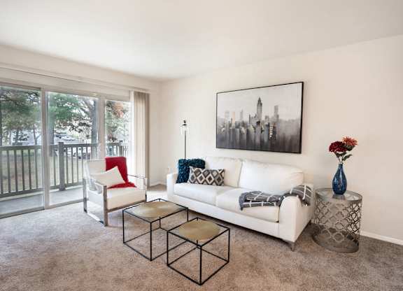 a living room with a white couch and chairs and a balcony at The Glendale Residence, Lanham