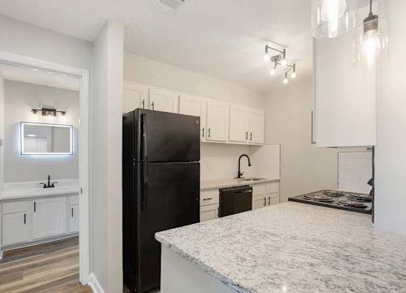A black refrigerator sits in a kitchen with white cabinets and a marble countertop at The Onyx Hoover Apartments, Alabama, 35216