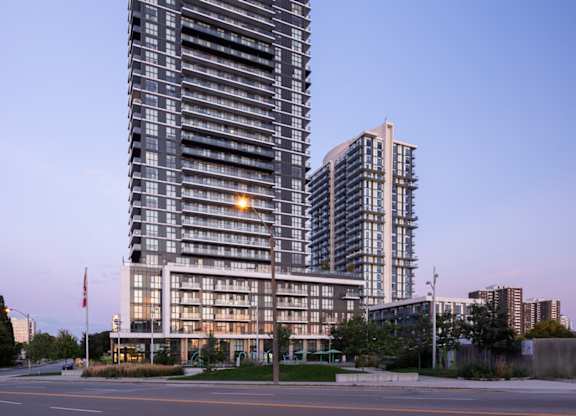 A tall, modern building with a curved top stands in the foreground with a clear blue sky above.