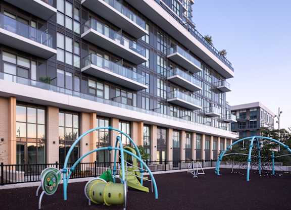 A playground with a slide and swings in front of a tall building.