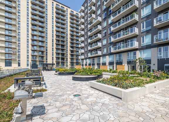 A courtyard with a stone floor and a planter area in front of apartment buildings.