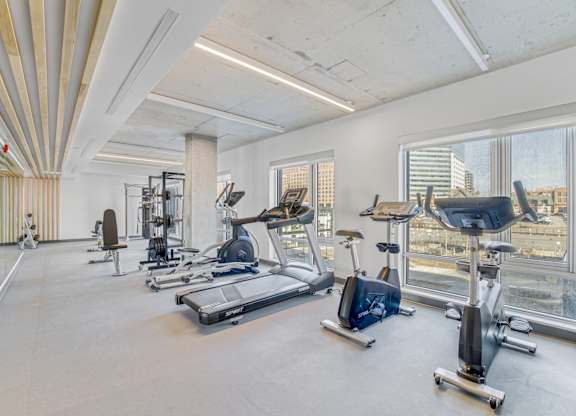 A spacious gym with a variety of exercise equipment and a view of the city skyline.
