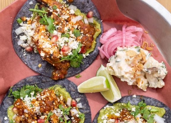 three tacos on a plate with 2 wedges of lime