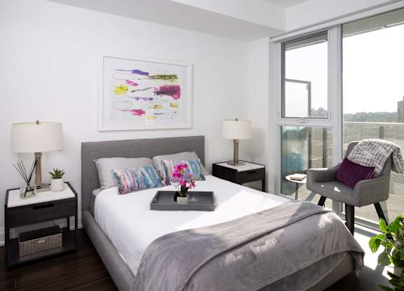 A bedroom with a large bed, two lamps, a painting, and a chair.