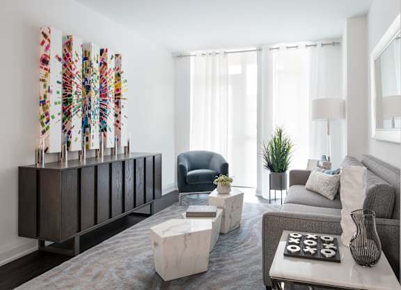 A living room with a grey couch, a white coffee table, and a wooden cabinet with a colorful decoration on top.