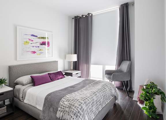 A bedroom with a large bed and a grey chair.