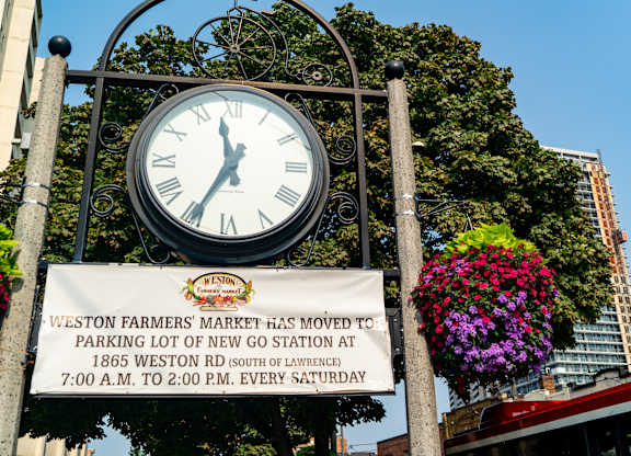 a large clock in front of a sign for the west end farmers market