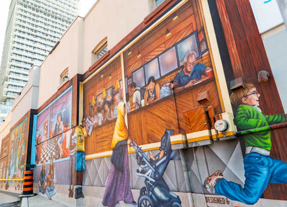 A mural on a building shows a man in a green shirt and blue jeans climbing a wall.