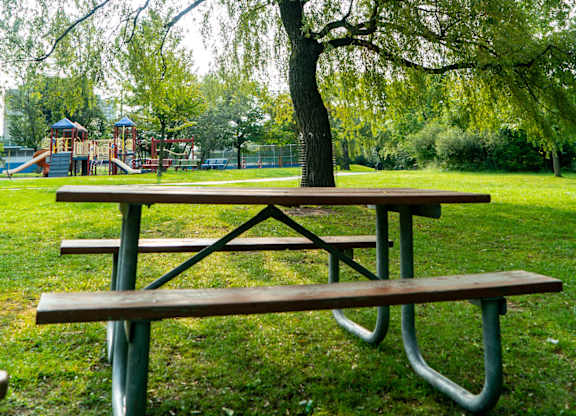 A picnic table and bench under a weeping willow tree in a park.