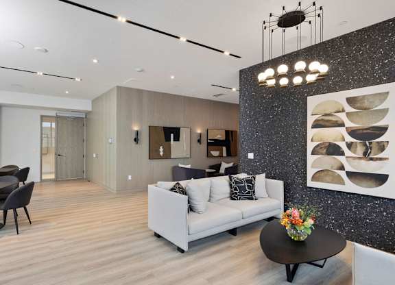 A modern living room with a grey sofa, a black coffee table, and a dining table with chairs.
