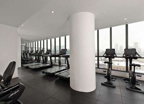 A gym with treadmills, exercise bikes and a large window.