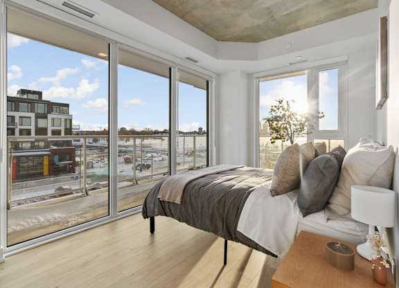 A bedroom with a large bed and a view of a cityscape through the windows.