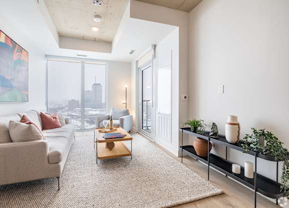 A living room with a couch, a coffee table, and a large window overlooking the city.