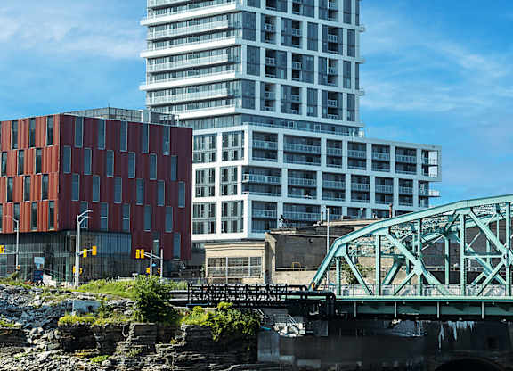 A modern glass building stands tall next to a red brick building with a bridge crossing a river in the foreground.