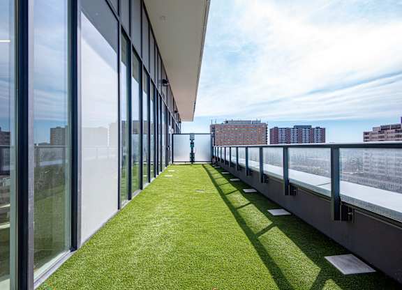 A long, narrow balcony with glass walls and a green lawn.