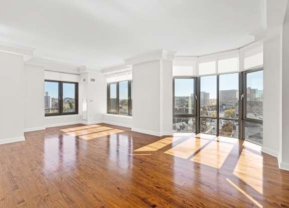 A large empty room with wooden floors and windows overlooking a cityscape.