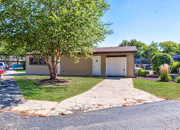 A small house with a driveway and a tree in front.