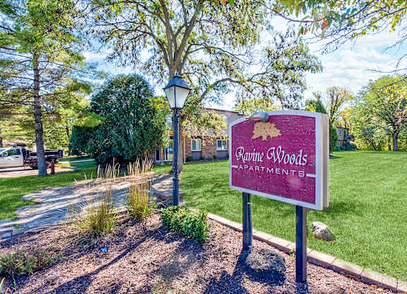 A sign for Ravine Woods Apartments stands in a grassy area.