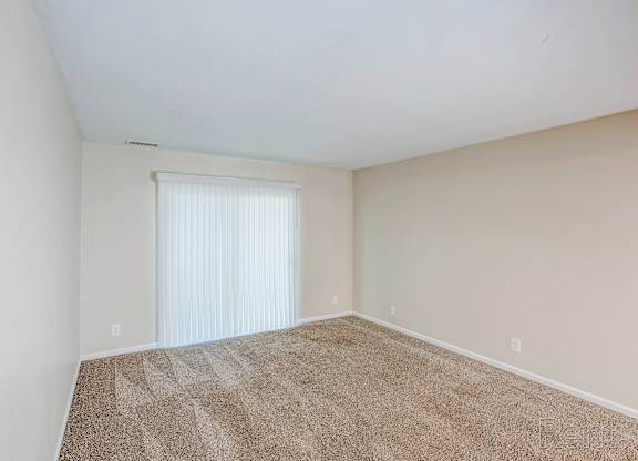 A room with a carpeted floor and a window with blinds.