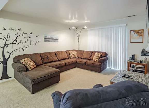 A living room with a large brown sectional sofa and a tree mural on the wall.