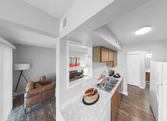 the kitchen and living room of an apartment with white walls and wood flooring