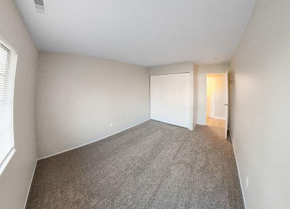 an empty bedroom with a carpeted floor and a door to a closet