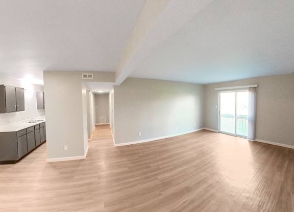 an empty living room with wood flooring and a kitchen