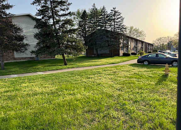 A grassy area in front of a building with a tree and a car parked on the side.