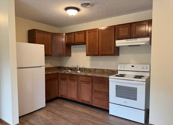 A kitchen with a white fridge, white stove, and brown cabinets.