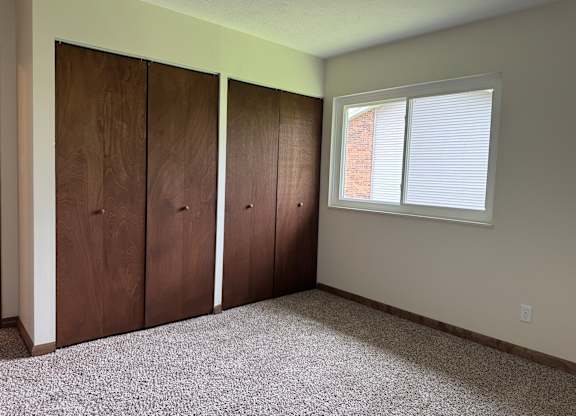A room with a window and three brown doors.