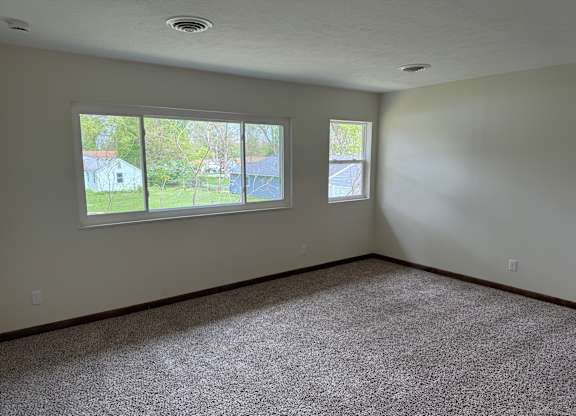 A room with a carpeted floor and two windows.