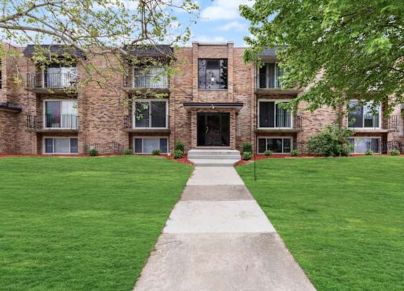exterior view of a brick apartment building with green grass and a sidewalk