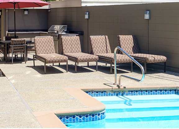 A pool with a red umbrella and chairs around it.