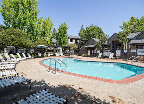 A pool surrounded by chairs and trees.