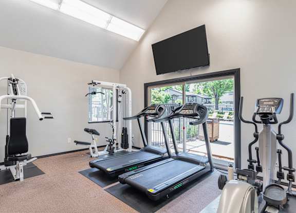A gym with treadmills, exercise bikes, and a television.
