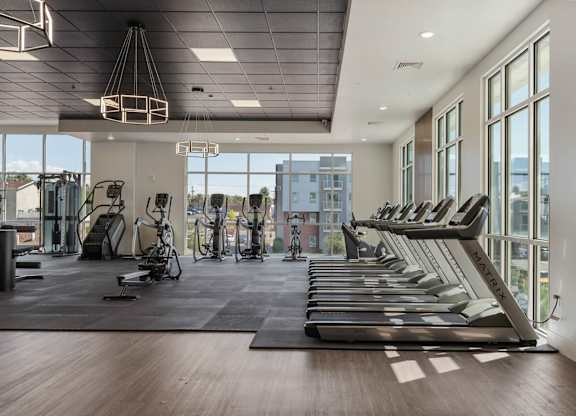 the gym with treadmills and windows at the district flats apartments at 605 Place Student Housing & Co-Living, Utah