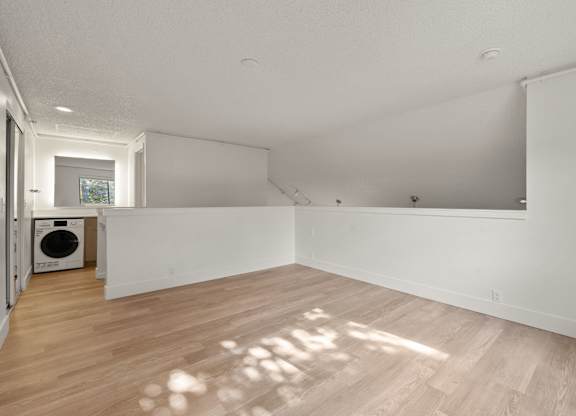 the living room and laundry room of a renovated house with white walls and wood floors at AVIA Lofts on Parkway Apartments, Washington, 98662